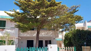 Un edificio residencial con un portón verde, un árbol en frente y un coche rojo estacionado cerca.