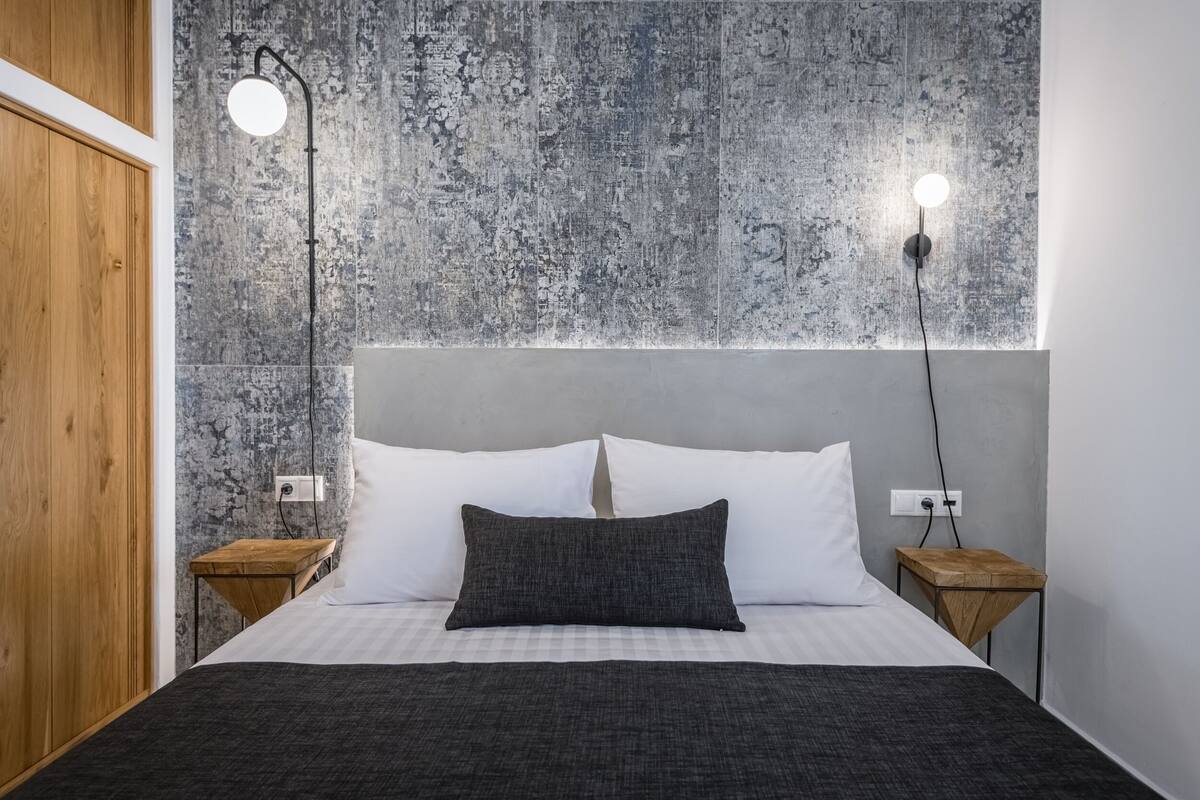 Un dormitorio con una cama, dos mesitas de noche, un armario de madera y una pared con textura.