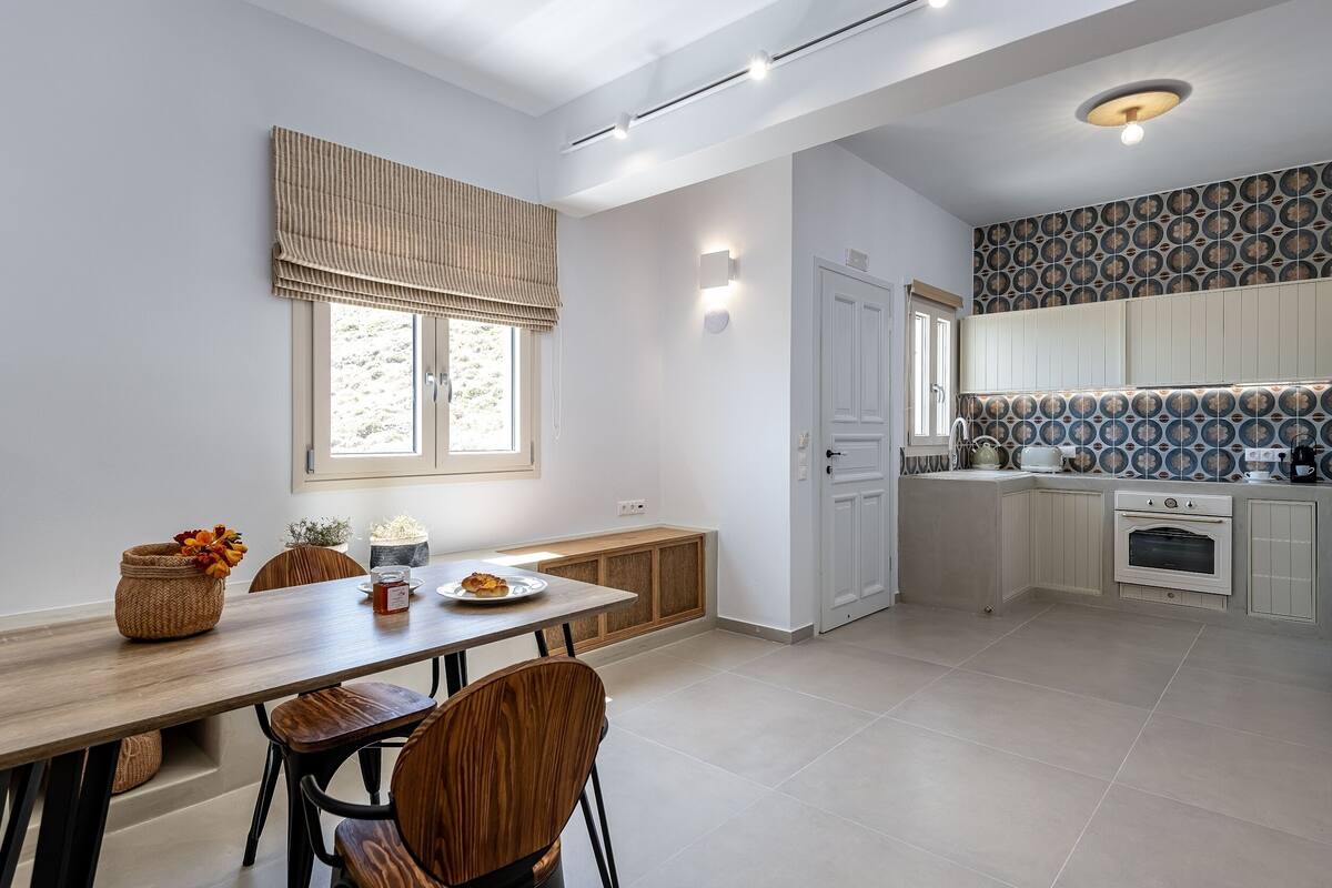 Una cocina moderna con armarios blancos, horno empotrado y ventana con persiana a rayas.