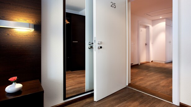 A hotel hallway with wooden flooring, white walls, and doors numbered 21 and 25. - Schlotzeria Hotel I Cafe I Eis (Grenzach-Wyhlen)