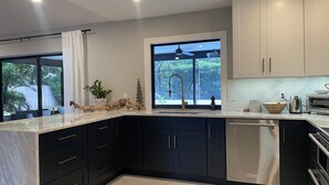 A modern kitchen with dark cabinets, a stainless steel dishwasher, and a window with a view of greenery. - Modern near Siesta Beach (Sarasota)