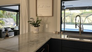 A modern kitchen with a marble countertop, a potted plant, and a framed welcome sign. - Modern near Siesta Beach (Sarasota)