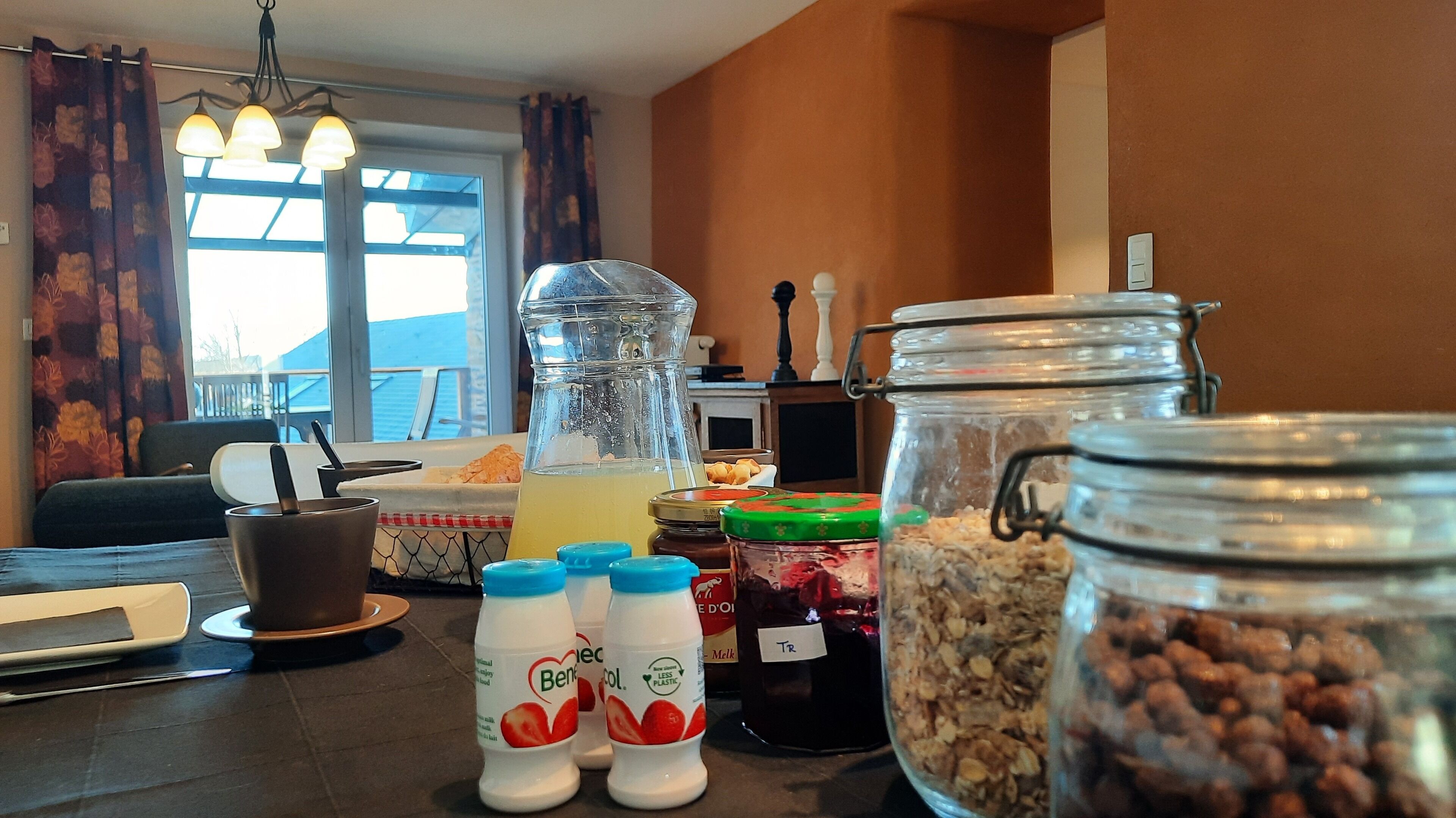 Une table dressée pour le petit-déjeuner, avec divers aliments et boissons, notamment une carafe, des pots et des bouteilles.