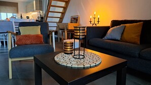 Ein modernes Wohnzimmer mit einem dunklen Sofa, einem Couchtisch mit dekorativer Unterlage und einer Treppe im Hintergrund.