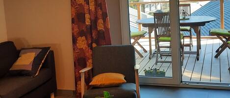 A living room with a sofa, a coffee table with a plant, and a view of an outdoor deck with a table and chairs.