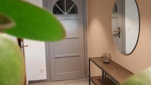 Ein Flur mit einer grauen Tür, einem runden Spiegel an der Wand und einem kleinen Tisch mit einem geometrischen Gegenstand darauf.