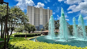 Um hotel com um edifício grande, uma fonte e vegetação bem cuidada.