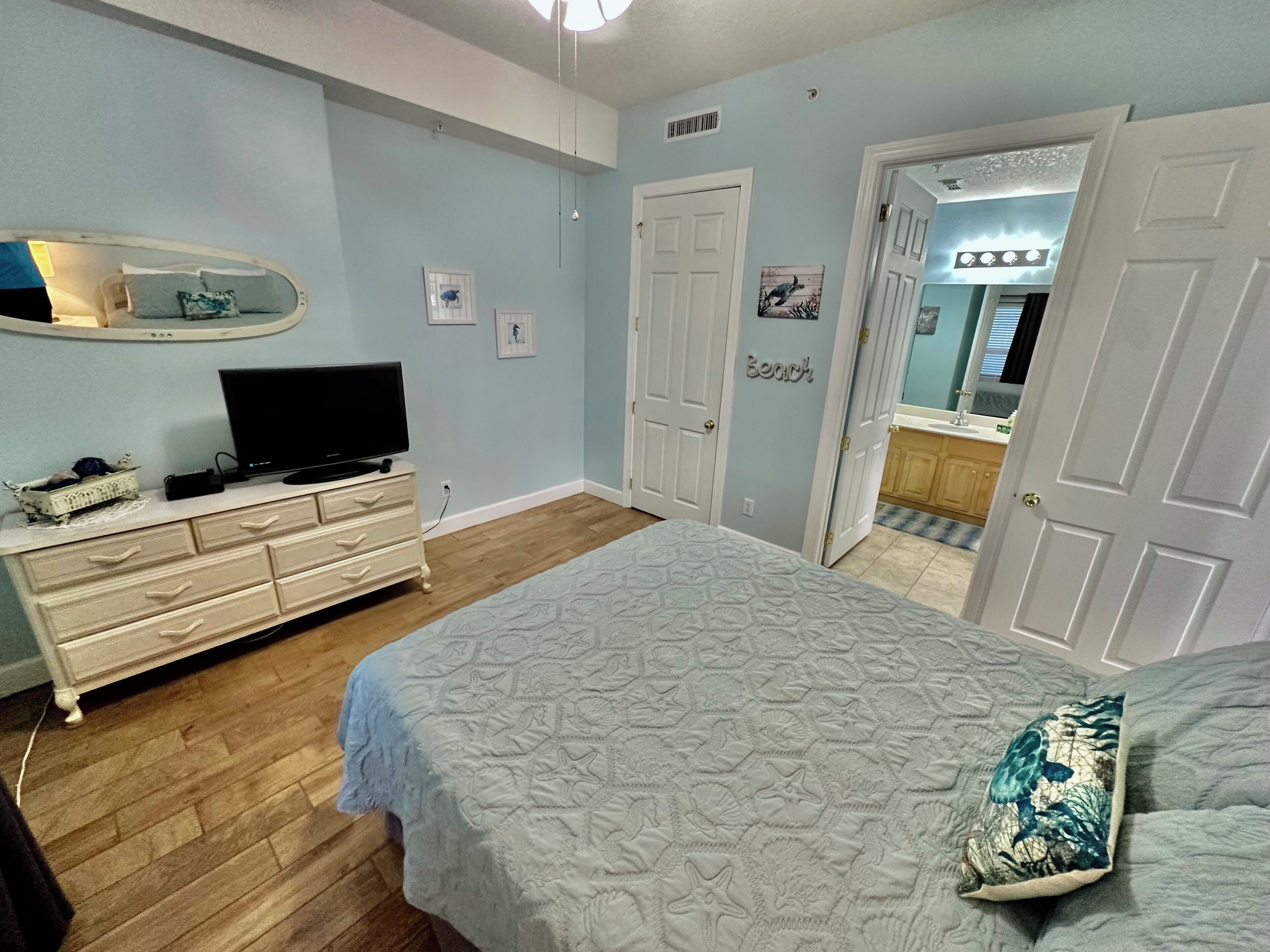 A bedroom with a bed, dresser, TV, and a bathroom visible through an open door.