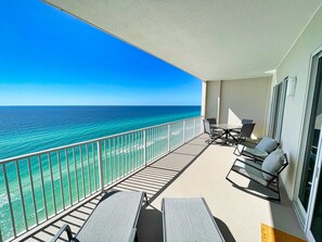 A balcony with a view of the ocean, a table with chairs, and a window. - Beach-Front Condo, Comfortable Recliners, XL Balcony, Free Beach Chairs! (Panama City Beach)