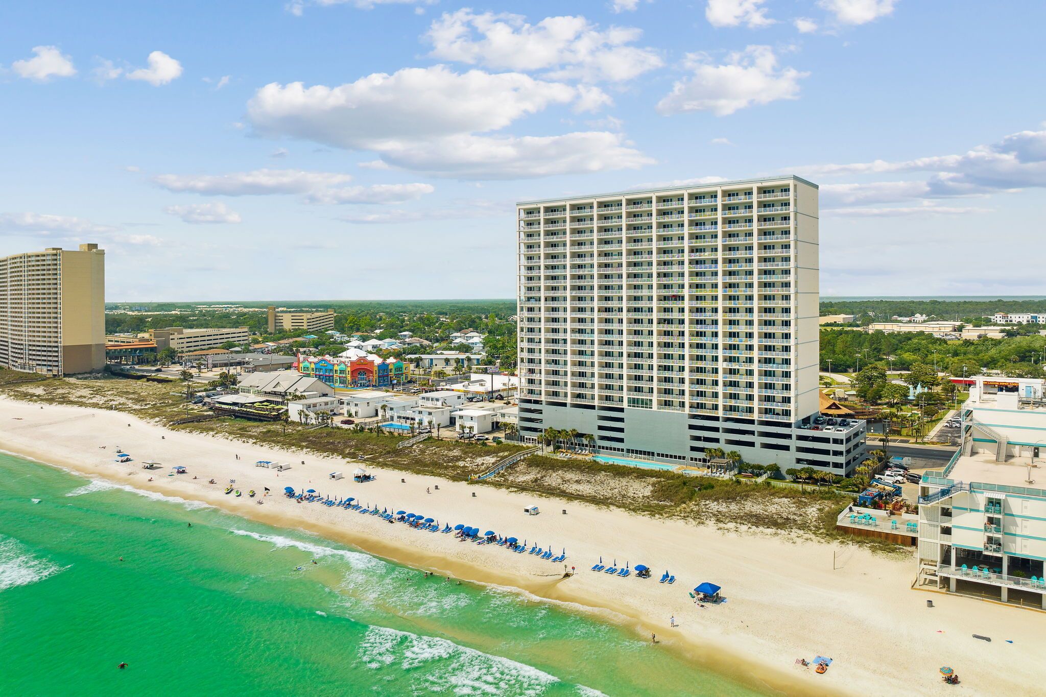 A beachfront hotel with a large building, a sandy beach, and clear turquoise waters.