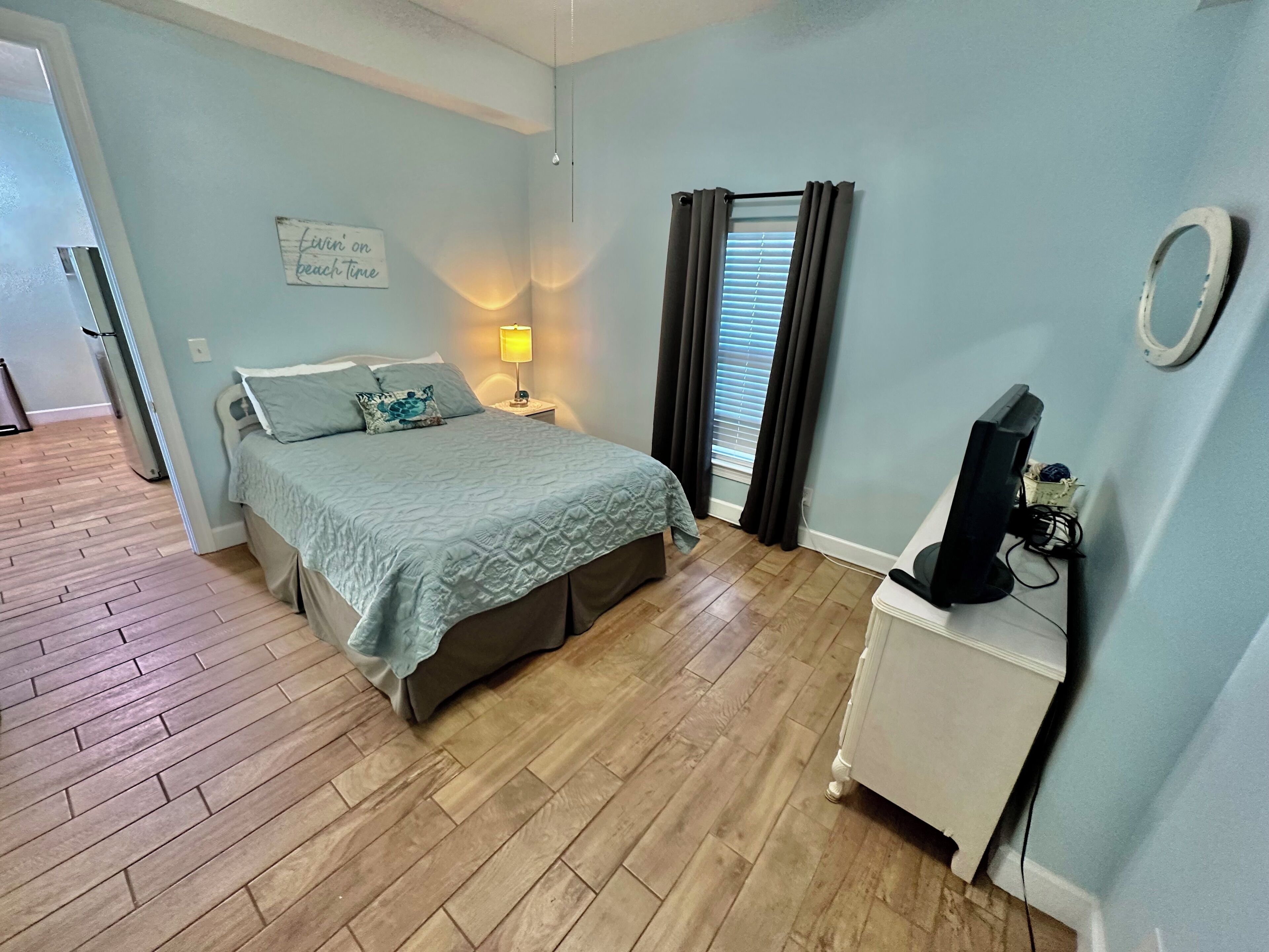 Un dormitorio con una cama, una mesita de noche con lámpara, un televisor y una ventana con cortinas.