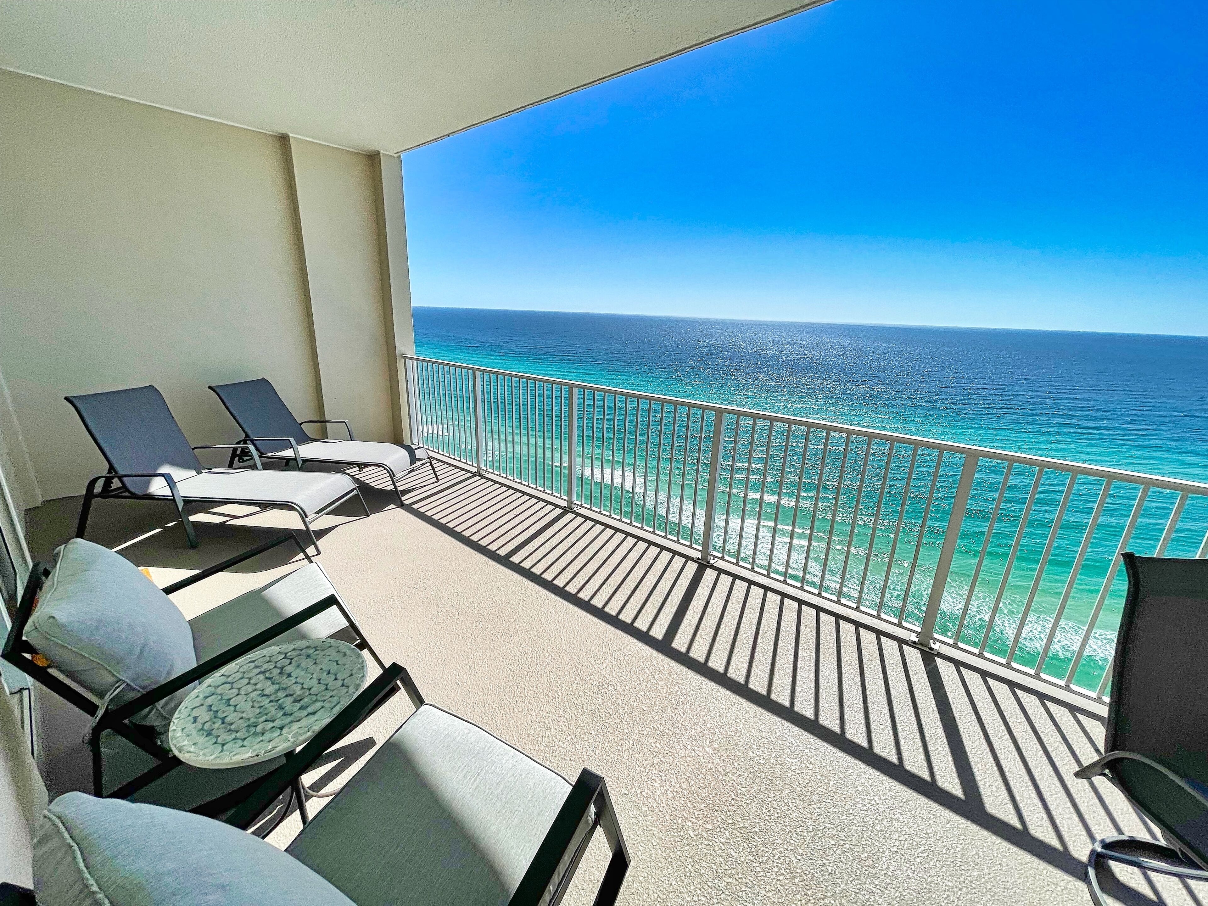 A balcony with two lounge chairs and a small table, overlooking a clear blue ocean.