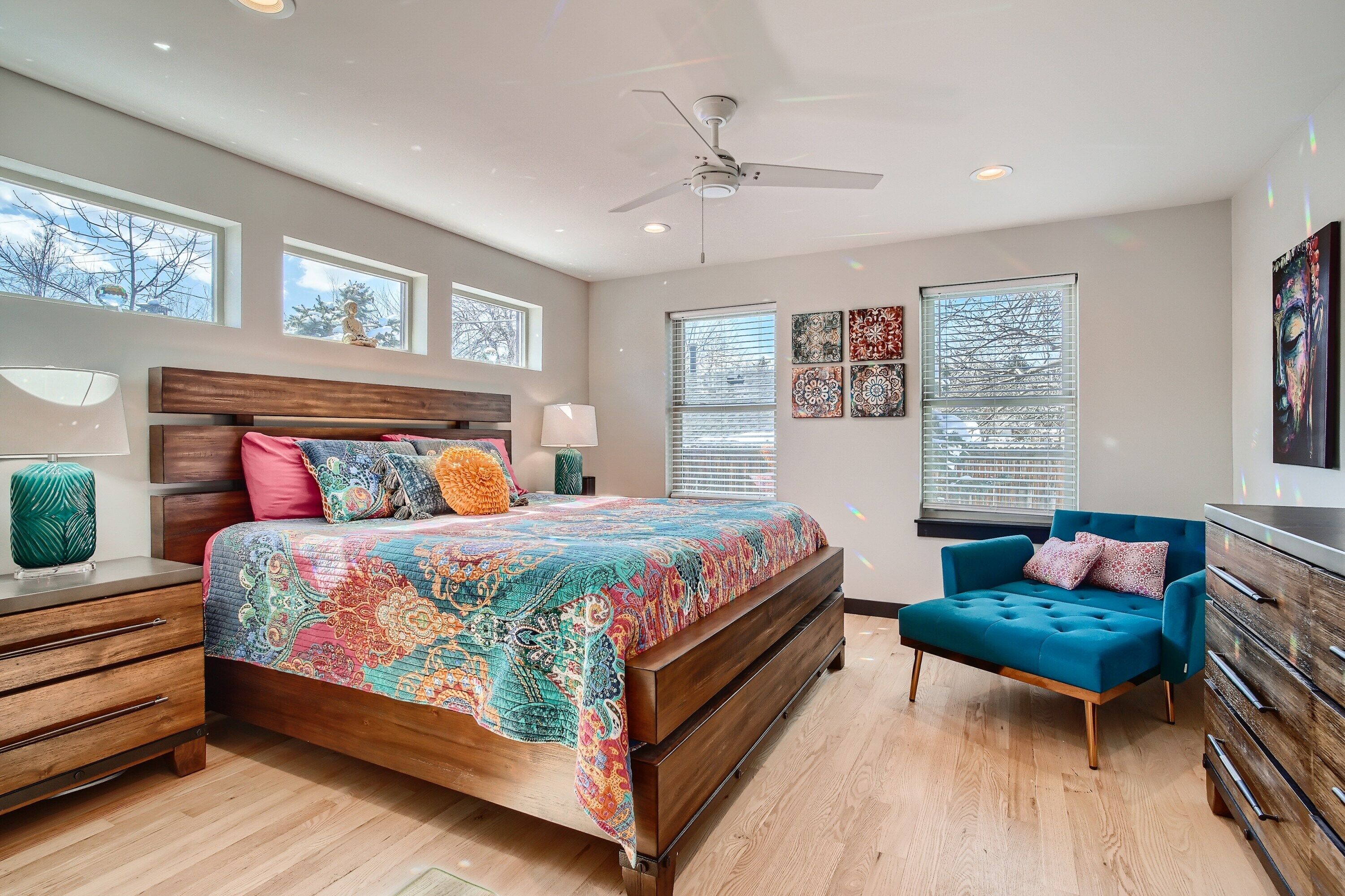 A bedroom with a large bed, a blue armchair, wooden nightstands, and a ceiling fan.