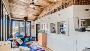 Una sala de estar acogedora con un sofá azul, un reposapiés morado y techo de madera.