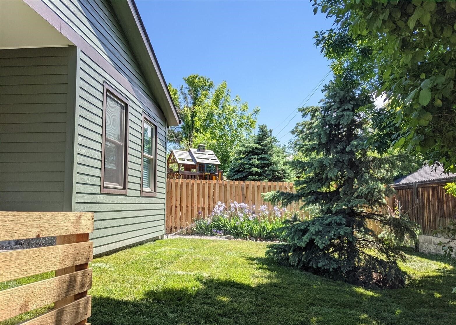 A house with a wooden deck, a fenced yard, and a small garden with flowers.