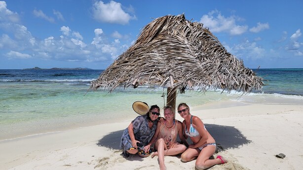 A beach scene with a thatched hut, clear blue water, and footprints in the sand. - 44-foot Luxury Catamaran "SeAtitudes" at Grande Anse Beach in Grenada. (Saint George's)