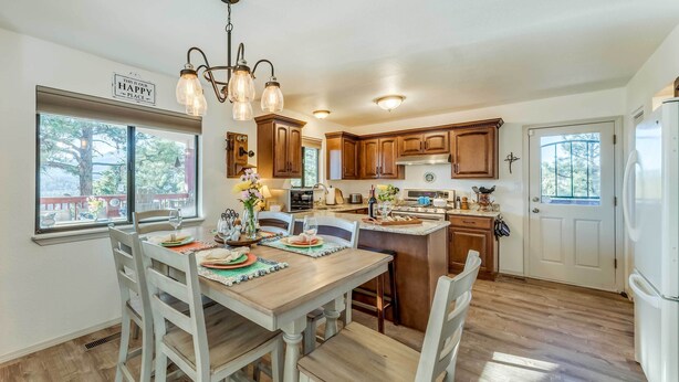 A kitchen with wooden cabinets, a dining table with chairs, a chandelier, and a refrigerator. - Wildlife Watching & Mtn Views: Luxe Ruidoso Escape (Ruidoso)