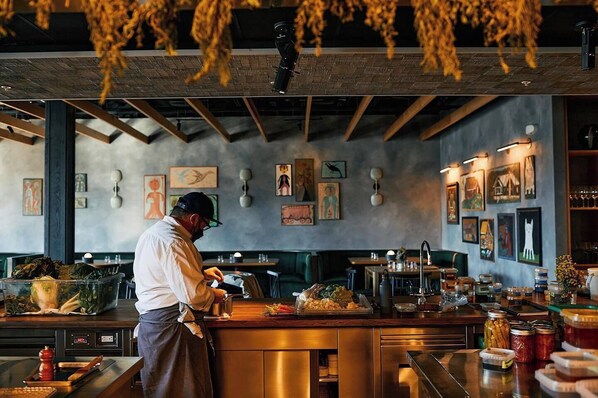 A chef preparing food in a restaurant with a modern interior, wooden ceiling, and artwork on the walls.