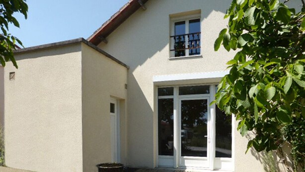 A building with a white exterior, a door, and a window. There is a potted plant to the left of the door.