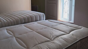 A bed with a quilted headboard and footboard, a window with a view, and a door to the right.