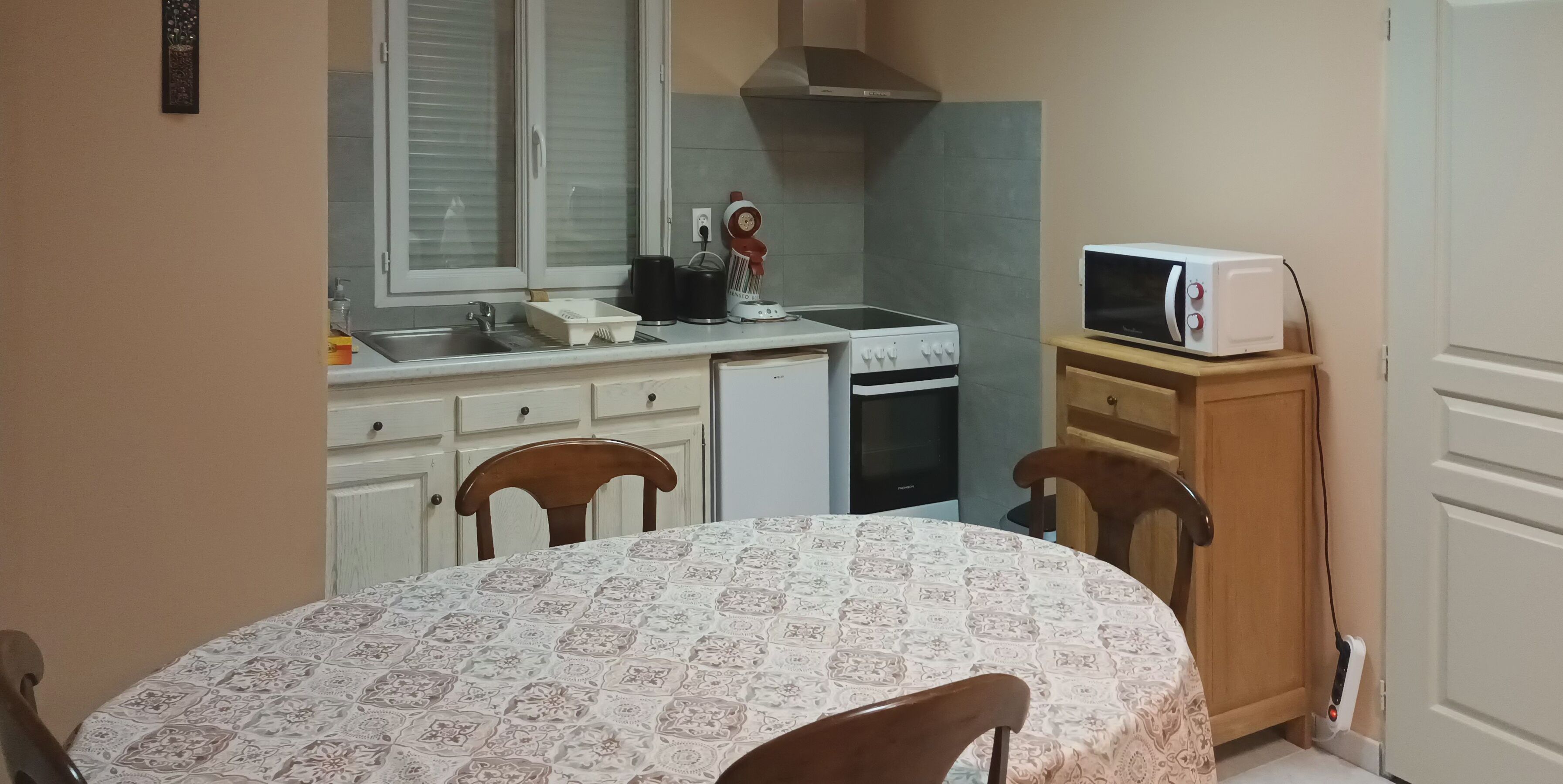 Una cucina compatta con piano cottura, forno a microonde e lavello. C'è un tavolo da pranzo con sedie e un mobile contenente un forno a microonde.