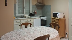 A compact kitchen with a stove, microwave, and sink. There is a dining table with chairs and a cabinet with a microwave on top.