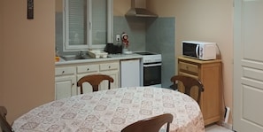 Une cuisine compacte équipée d’une cuisinière, d’un four à micro-ondes et d’un évier. On y trouve une table à manger avec des chaises, ainsi qu’un meuble sur lequel est posé un four à micro-ondes.