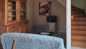 A living room with a wooden staircase, a dining area with a cabinet, and a painting on the wall.