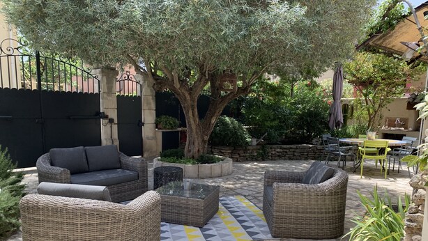 An outdoor seating area with wicker furniture and a stone floor, surrounded by greenery and a tree. - Aix en Provence has quiet house 5m from the city center on foot (Aix-en-Provence)
