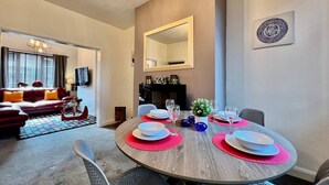 A dining area with a round table set for four, a sofa in the background, and a mirror on the wall. - Johnson House - Contractors, Families, Holidays (Cleethorpes)