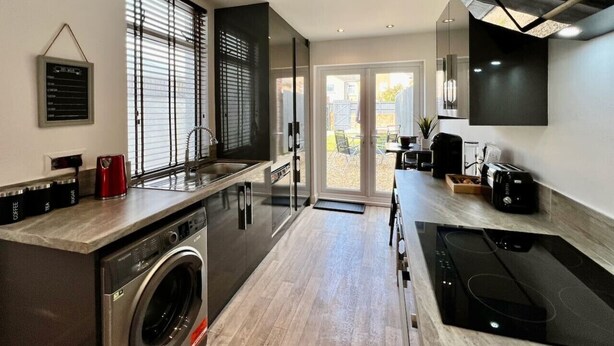A modern kitchen with a built-in washing machine, a large window with blinds, and a flat-screen TV mounted on the wall. - Johnson House - Contractors, Families, Holidays (Cleethorpes)