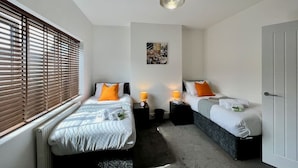 A bedroom with two beds, a ceiling light, a wall clock, and a door. - Johnson House - Contractors, Families, Holidays (Cleethorpes)