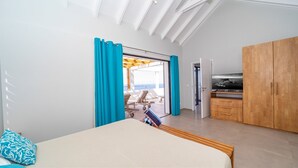 Une chambre avec un lit, une télévision et une vue sur la mer, visible par la porte.