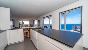 A modern kitchen with a large island, white cabinetry, and a view of the ocean. - Belharra Luxury villa (Gustavia)