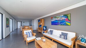 A modern living room with a sofa, coffee table, and chairs. There is a bookshelf and a painting on the wall. - Belharra Luxury villa (Gustavia)