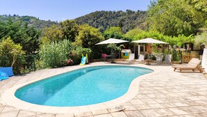 A swimming pool with a tiled deck, surrounded by greenery and a hillside. - A bit of straw (Cagnes-sur-Mer)