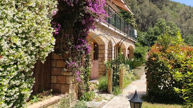 A stone building with a balcony, surrounded by lush greenery and flowering plants. - A bit of straw (Cagnes-sur-Mer)