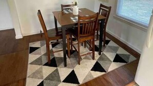Een eetruimte met een houten tafel en stoelen, een kamerbreed tapijt met een patroon, en een hanglamp.