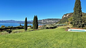 A well-maintained lawn with tall cypress trees, a swimming pool, and a view of a lake and mountains. - Stunning new villa with beautiful lake view (Bardolino)