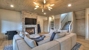 A cozy living room with a stone fireplace, a sectional sofa, and a ceiling light fixture. - 4 Dancing Bears|Mtn Views+Hot Tub+ Design (Blue Ridge)