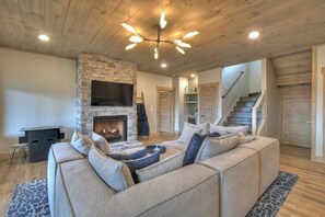 A cozy living room with a stone fireplace, a sectional sofa, and a ceiling light fixture. - 4 Dancing Bears|Mtn Views+Hot Tub+ Design (Blue Ridge)
