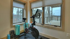 A room with a stationary bike, exercise mats, and large windows with blinds. - 4 Dancing Bears|Mtn Views+Hot Tub+ Design (Blue Ridge)