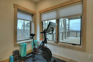 A room with a stationary bike, exercise mats, and large windows with blinds. - 4 Dancing Bears|Mtn Views+Hot Tub+ Design (Blue Ridge)