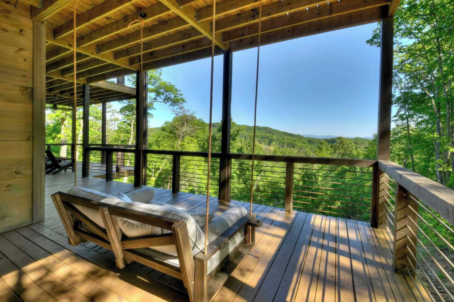 A wooden deck with a bed and a view of a forested landscape.