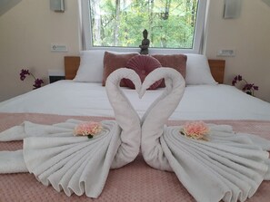 A hotel room with a bed featuring a swan towel arrangement and a view of trees through the window. - Villa Melani (Oriovac)