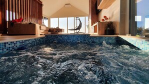 A modern indoor swimming pool with a jacuzzi, wooden deck, and a large window providing a view of the outdoors. - Villa Melani (Oriovac)