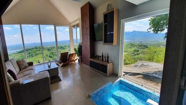 A modern living room with a large window, a pool, and a sofa. - Villa Melani (Oriovac)