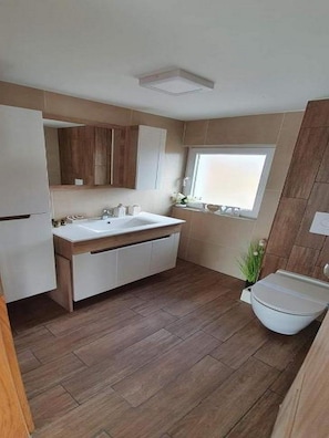 A modern bathroom with a white sink, wooden cabinets, and a window providing natural light. - Villa Melani (Oriovac)