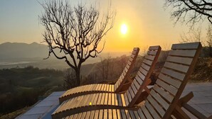 A wooden bench with a curved backrest, positioned on a concrete ledge overlooking a landscape with a tree and mountains in the distance. - Villa Melani (Oriovac)