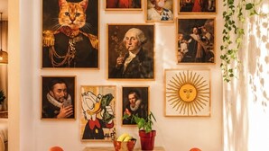 Ein Essbereich mit einem Holztisch und orangenen Stühlen, umgeben von verschiedenen gerahmten Kunstwerken an der Wand.